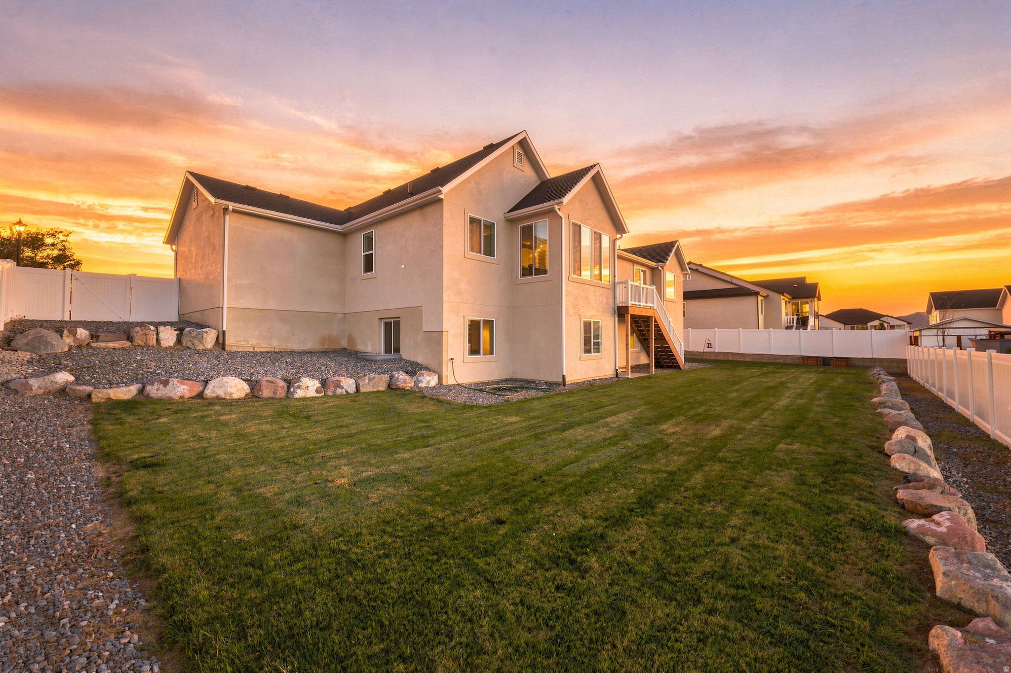 Expansive backyard featuring a manicured lawn, white vinyl fencing, and a gravel pathway with rock borders