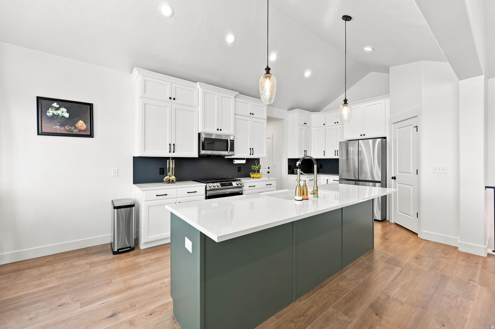 Bright kitchen featuring white cabinetry, a large center island with a white countertop, stainless steel appliances, and wood-finish flooring