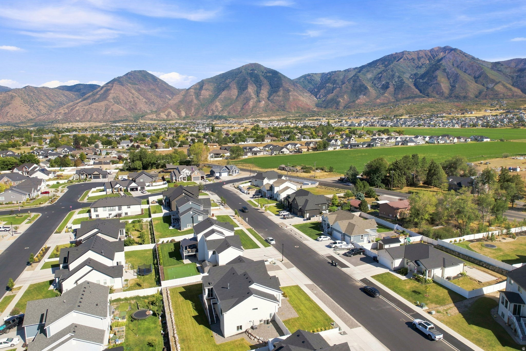 Aerial perspective showcasing a residential community with paved streets, surrounded by expansive green fields and distant mountains