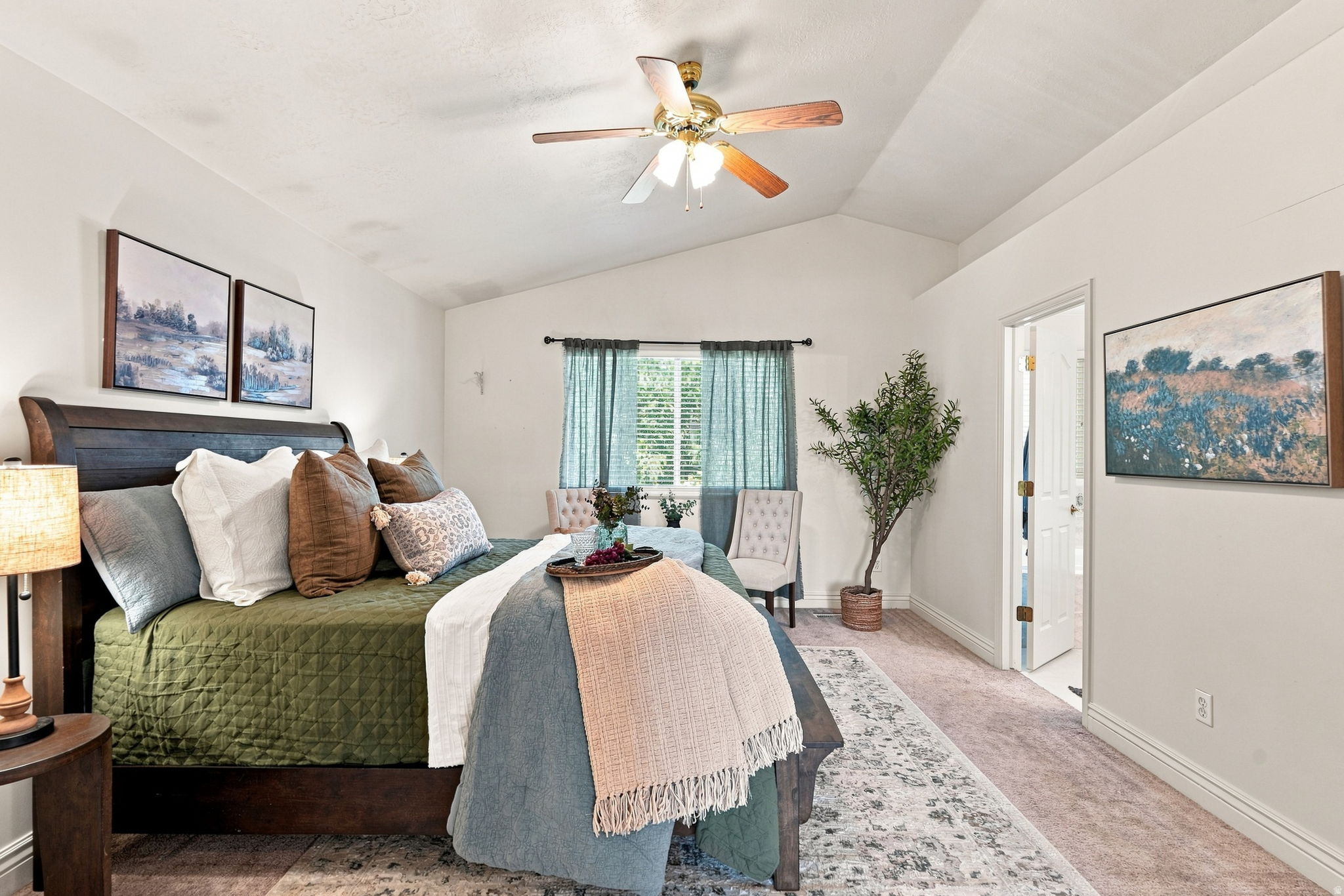Primary bedroom suite featuring a vaulted ceiling with ceiling fan, wood-finish flooring, and expansive windows with light filtering curtains