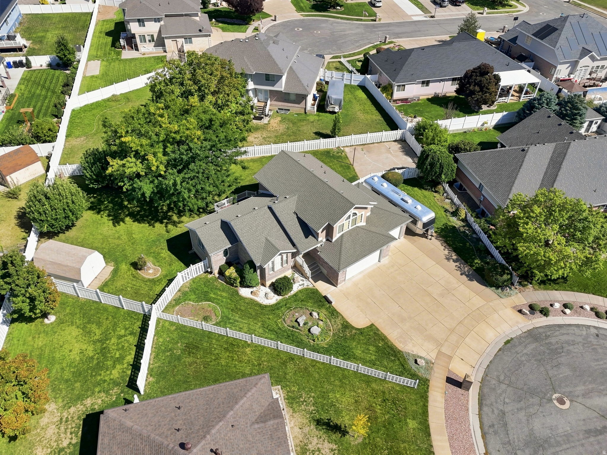 Expansive property featuring a multi-gable roofline, a concrete driveway, a white picket fence, and a storage shed