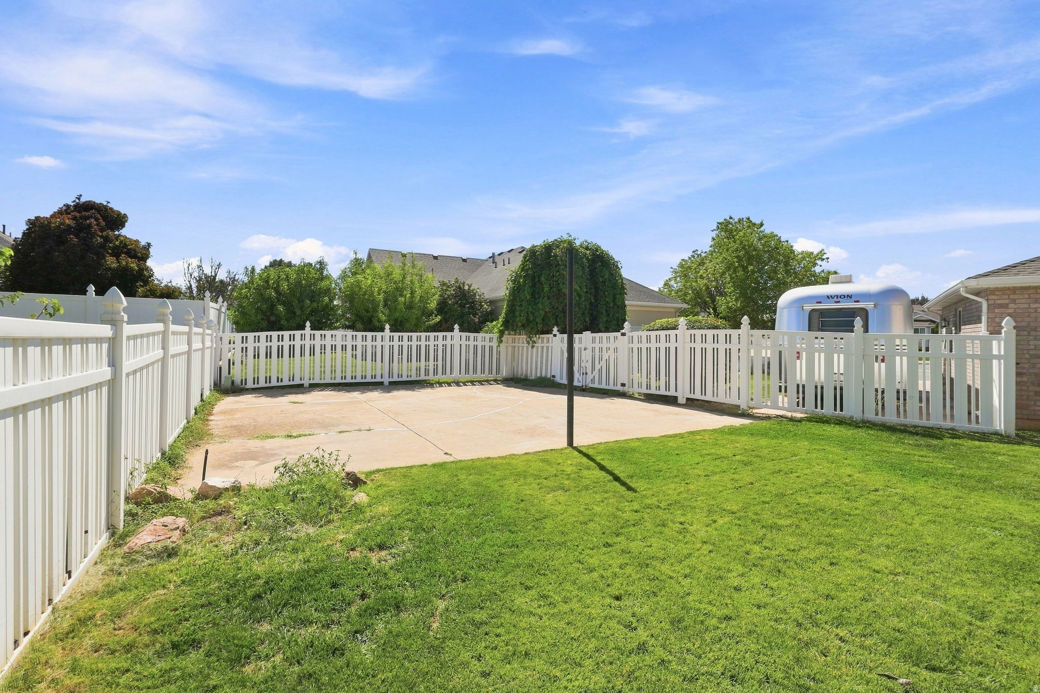 Expansive yard featuring a manicured lawn, a concrete patio area, and white picket fencing