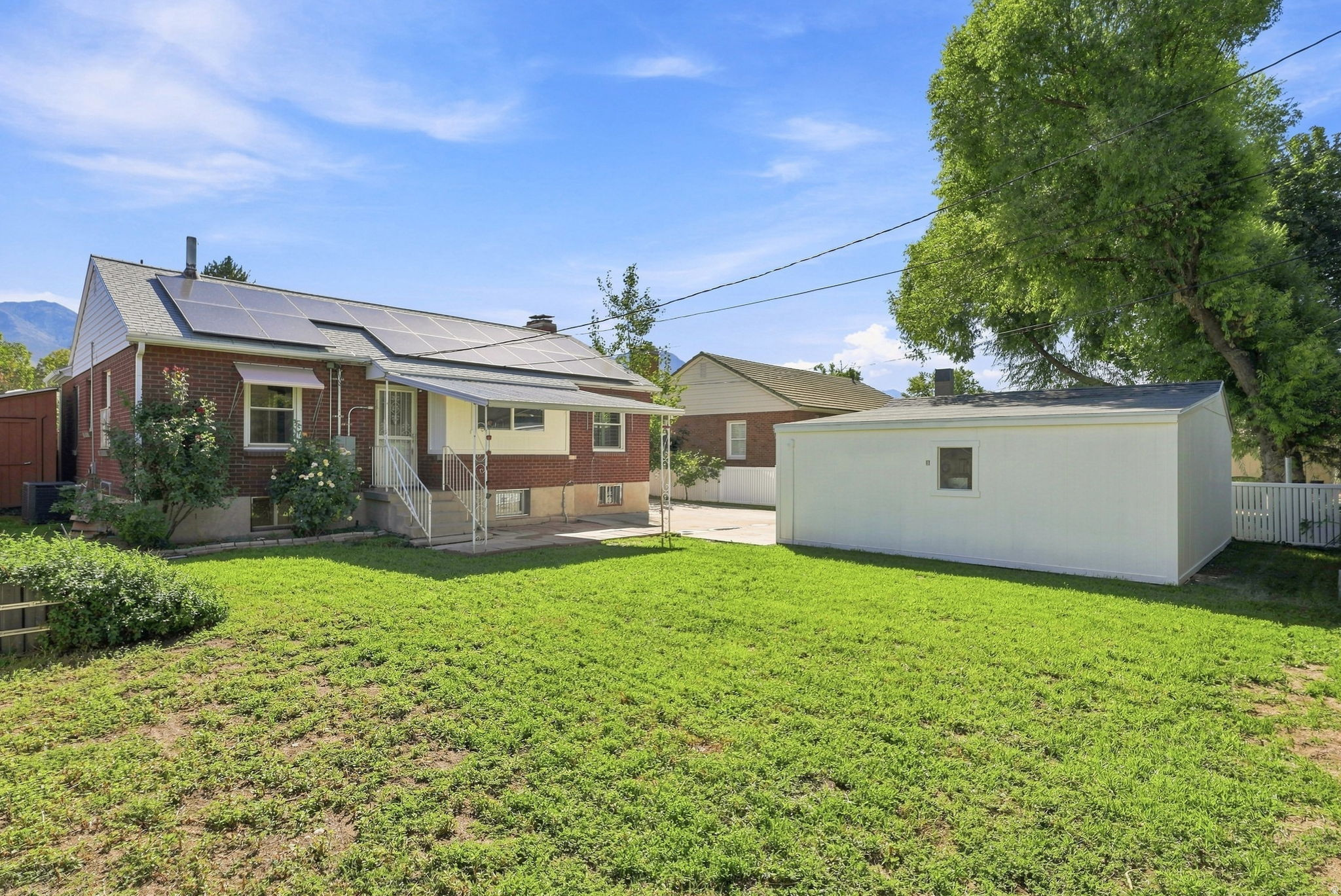 Expansive lawn area with a brick exterior residence, featuring solar panels and a covered patio