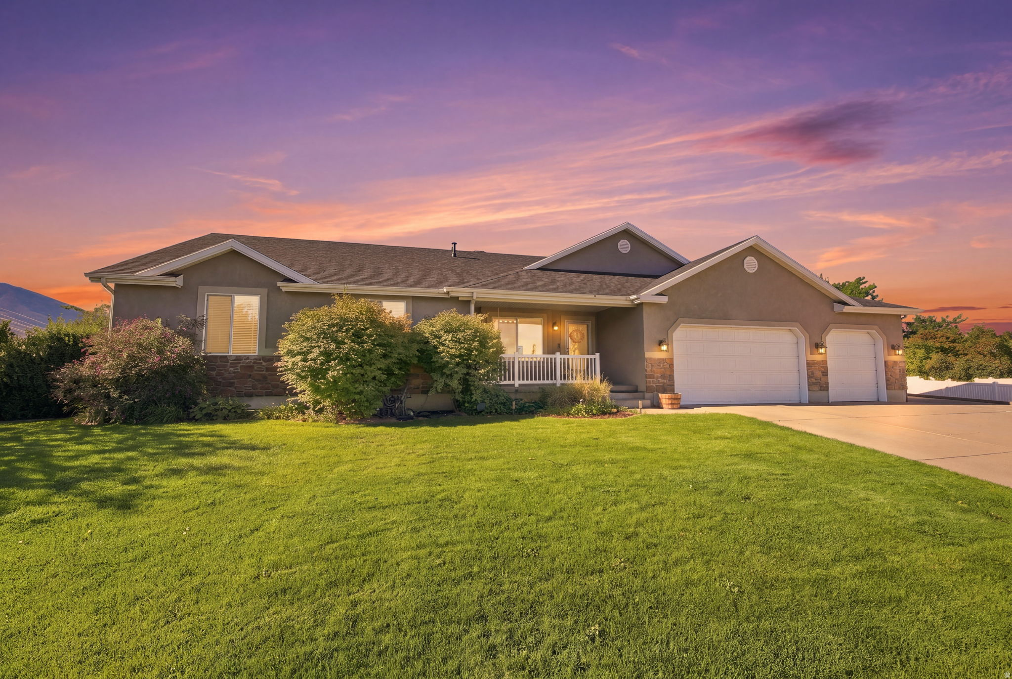 Stucco exterior with stone accents, a covered front porch with white railing, and a multi-car garage with white doors