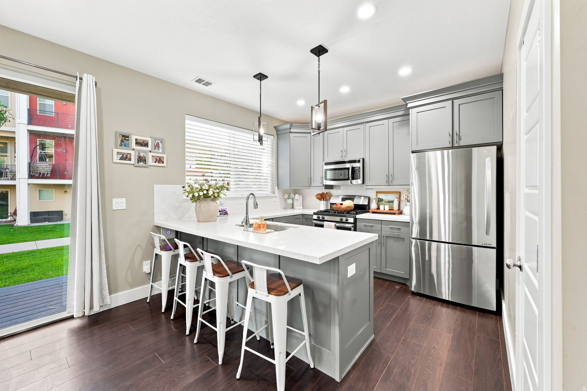 Modern kitchen featuring a large island with white countertop, gray cabinetry, stainless steel appliances, and dark wood-finish flooring