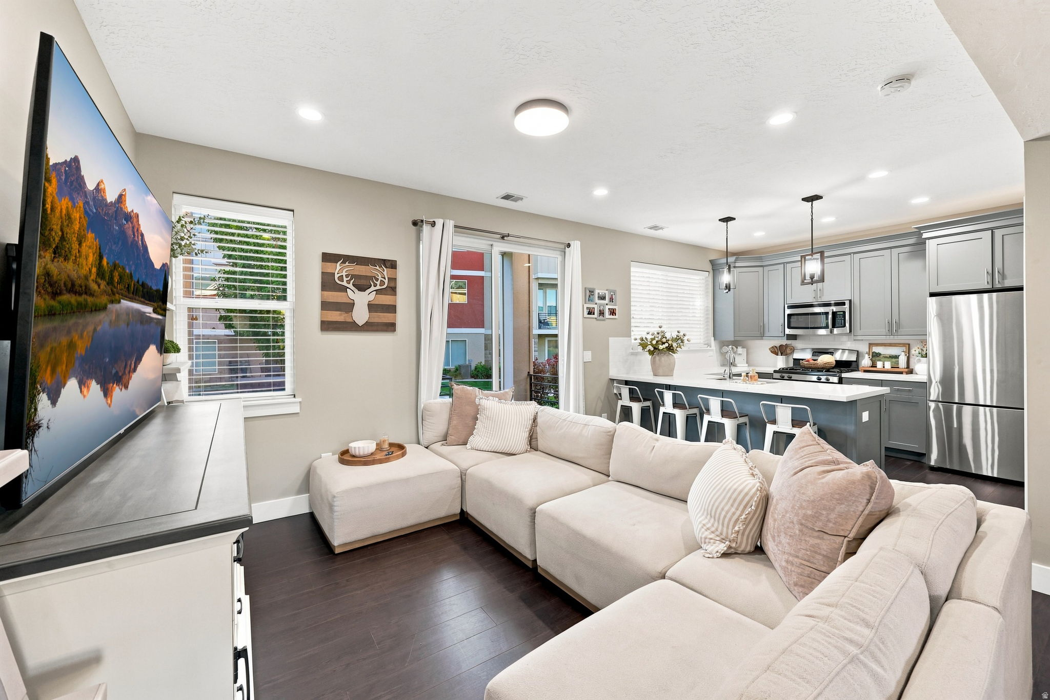 Open-concept living space featuring wood-finish flooring, recessed lighting, and a kitchen with gray cabinetry, an island, and stainless steel appliances