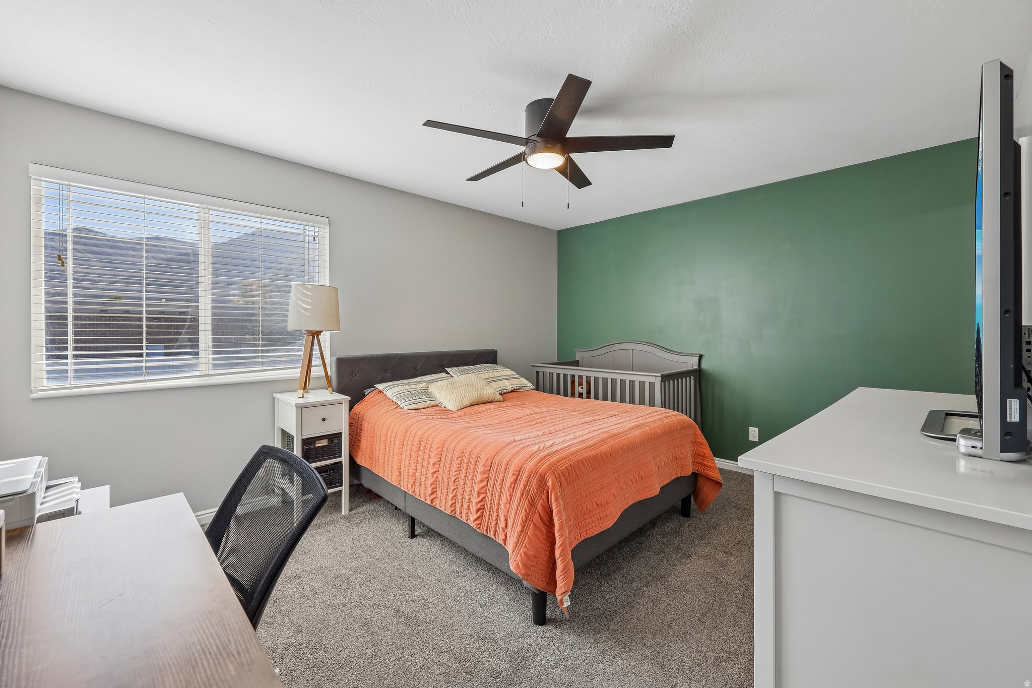 Carpeted bedroom featuring a large window, a ceiling fan, and an accent wall