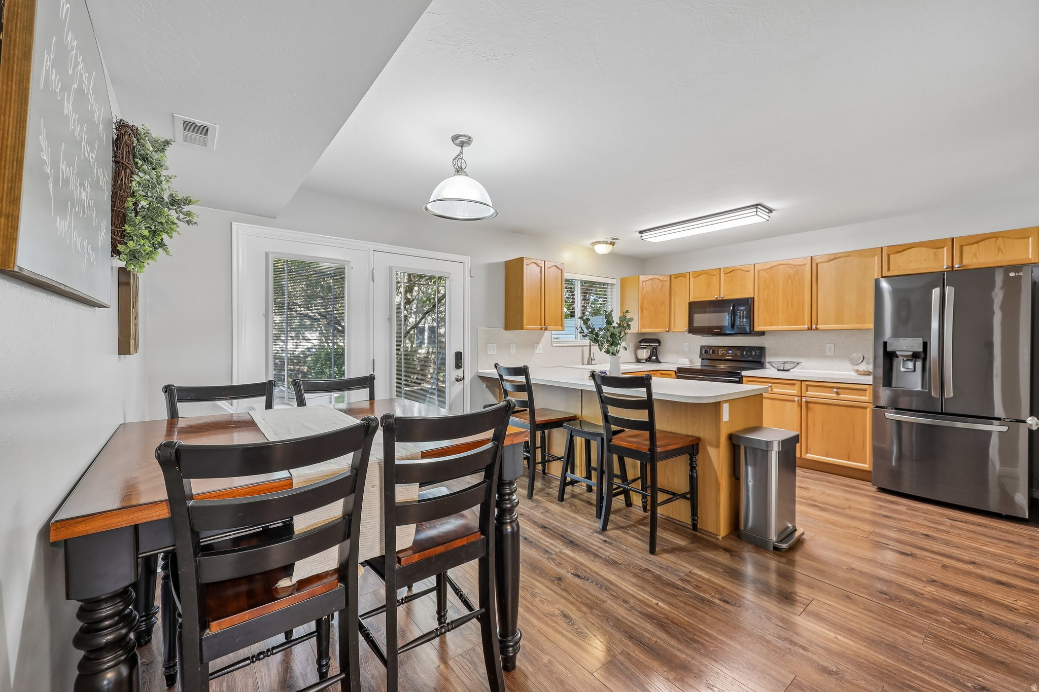 Wood-finish flooring throughout, kitchen with light wood cabinetry, stainless steel refrigerator, and white countertops