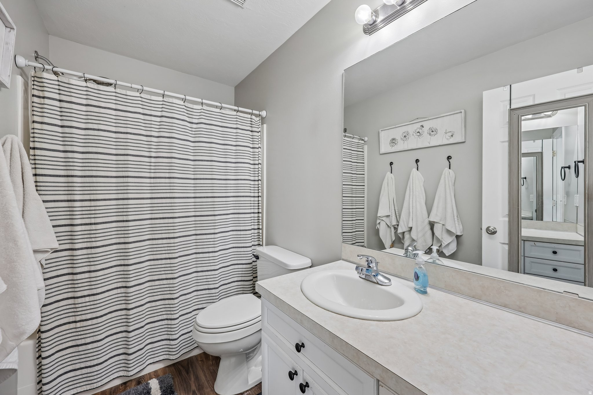 Bathroom featuring a single vanity with an integrated sink, broad wall-mounted mirror, and wood-finish flooring