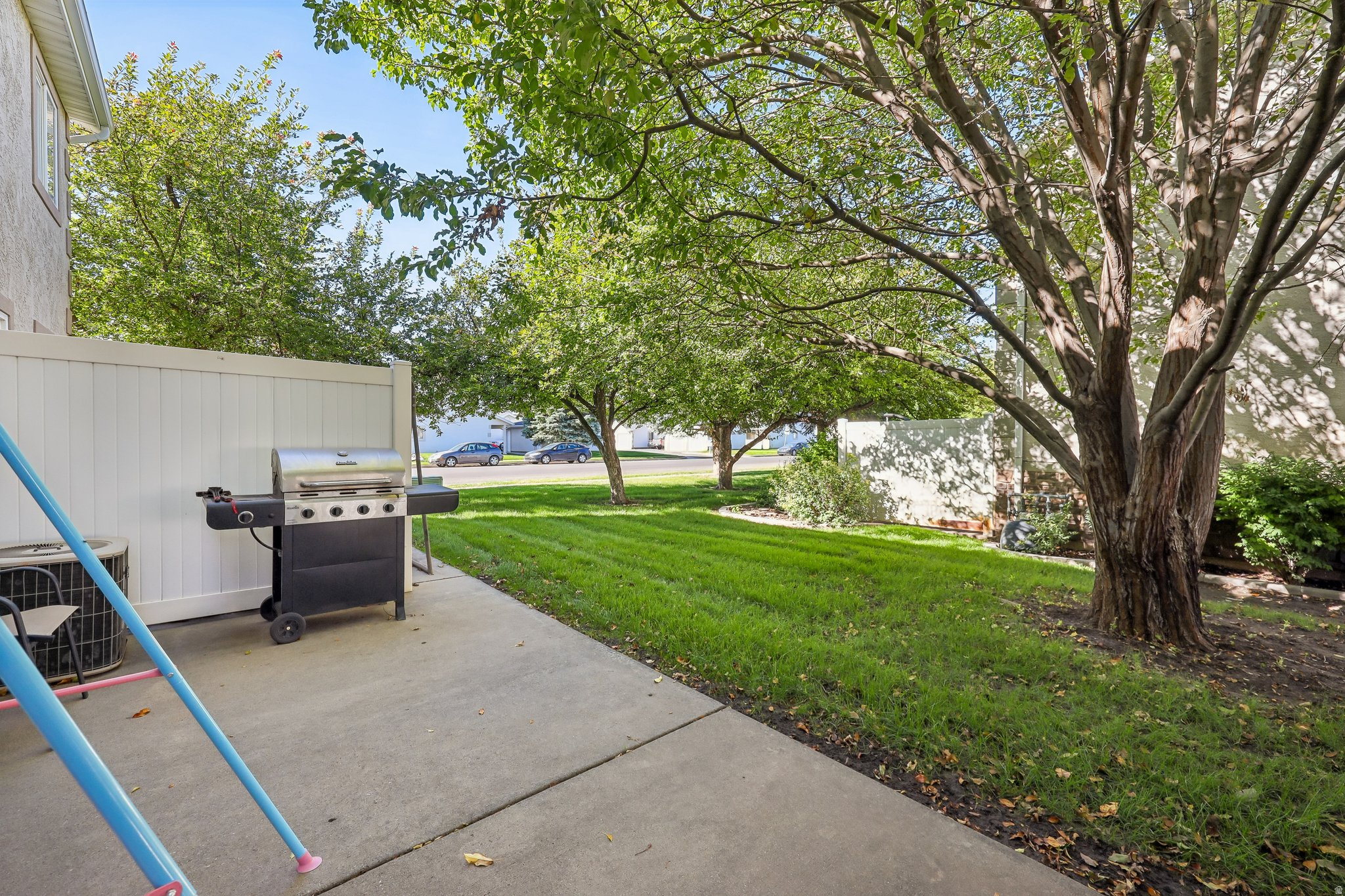 Patio area with a concrete surface, white privacy fencing, and a surrounding lawn with mature trees