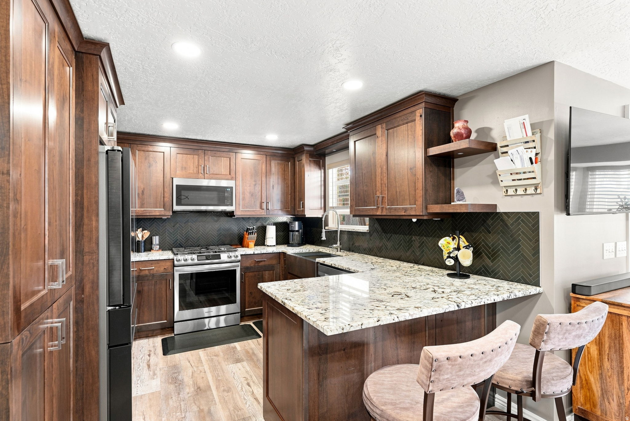 Kitchen featuring cherrywood cabinetry, stainless steel appliances, speckled stone-finish countertops, herringbone-patterned tile backsplash, and recessed lighting