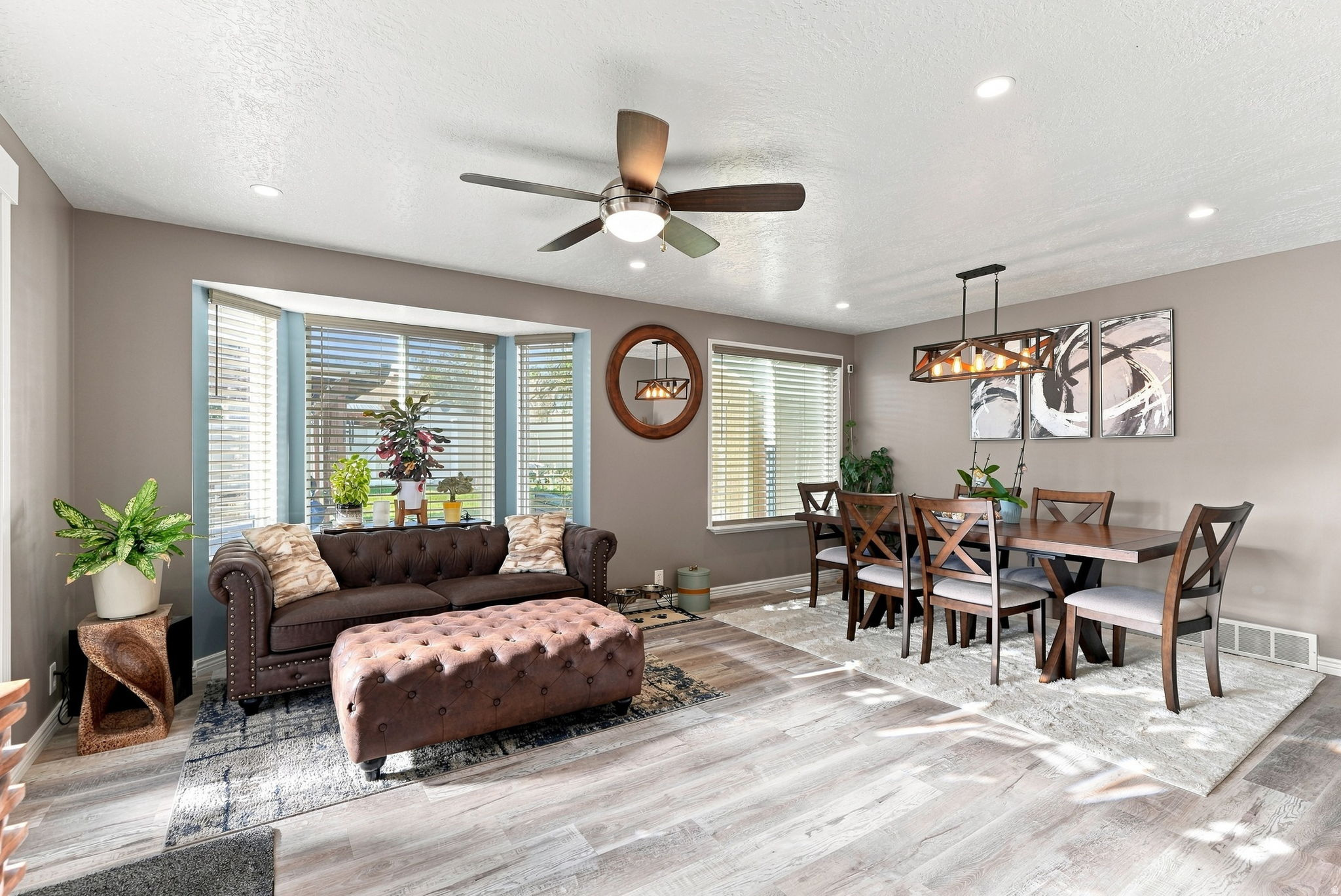 Expansive living and dining areas featuring wood-finish flooring, a bay window with blinds, recessed lighting, and a ceiling fan