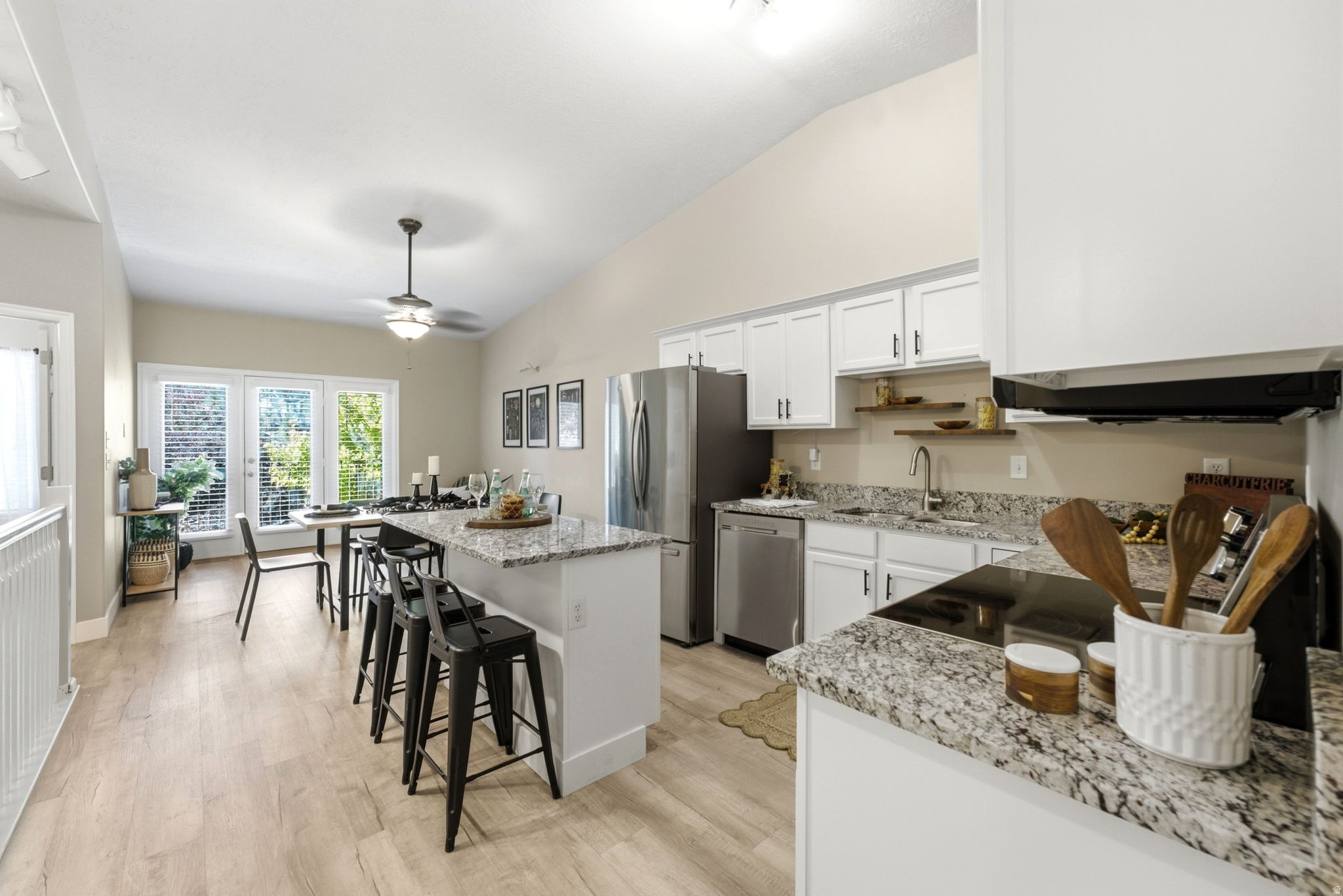 Open-concept kitchen featuring wood-finish flooring, white cabinetry, granite countertops, and stainless steel appliances