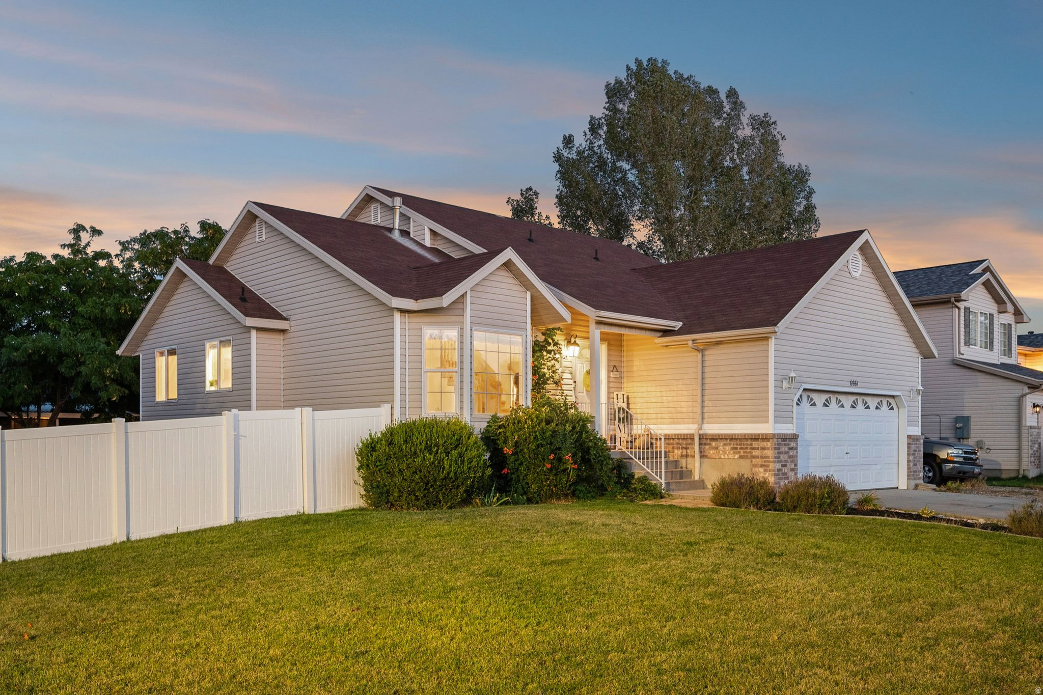 Vinyl siding exterior with a stone veneer accent, attached garage, front lawn, and a white privacy fence