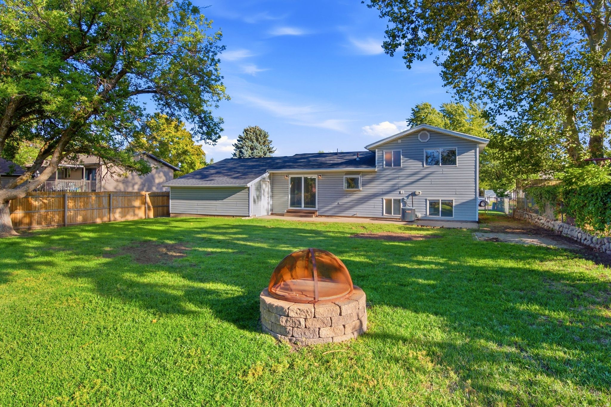Expansive backyard featuring a stone fire pit, mature trees, and a privacy fence