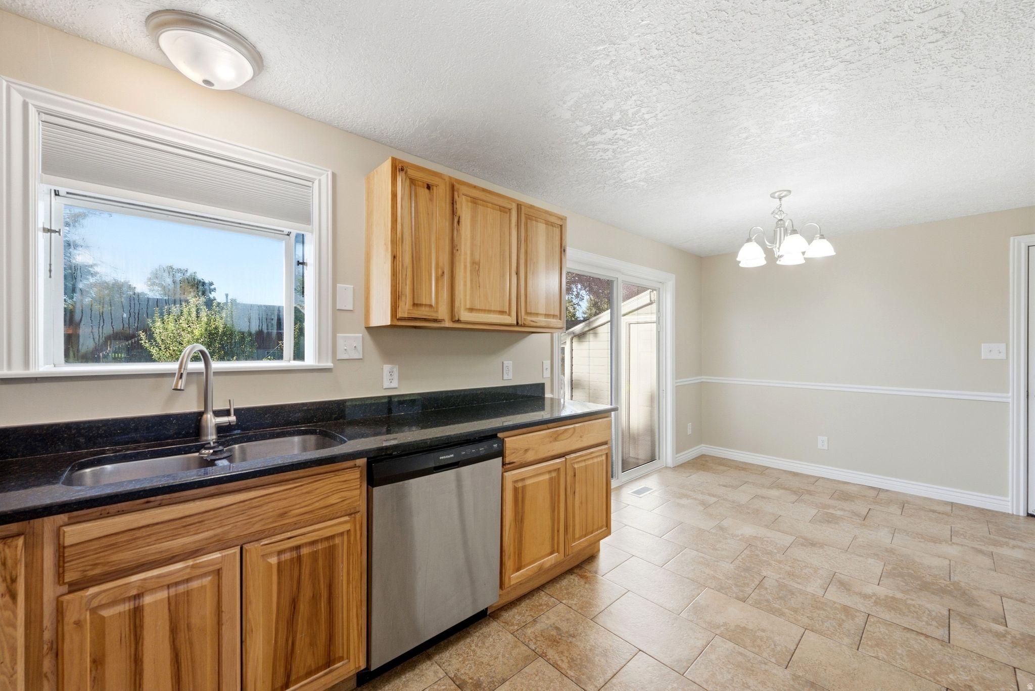 Kitchen with wood cabinetry, dark countertops, stainless steel sink, and a stainless steel dishwasher