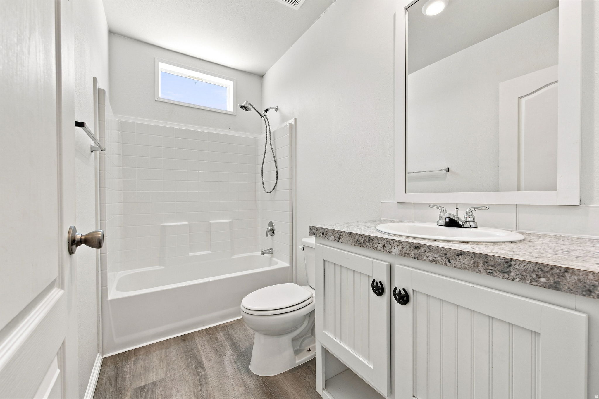 Spa-inspired bathroom featuring a frameless glass-enclosed shower with subway tile surround, dual vanity with quartz countertop and brushed nickel hardware, porcelain toilet, and wood-finish flooring throughout