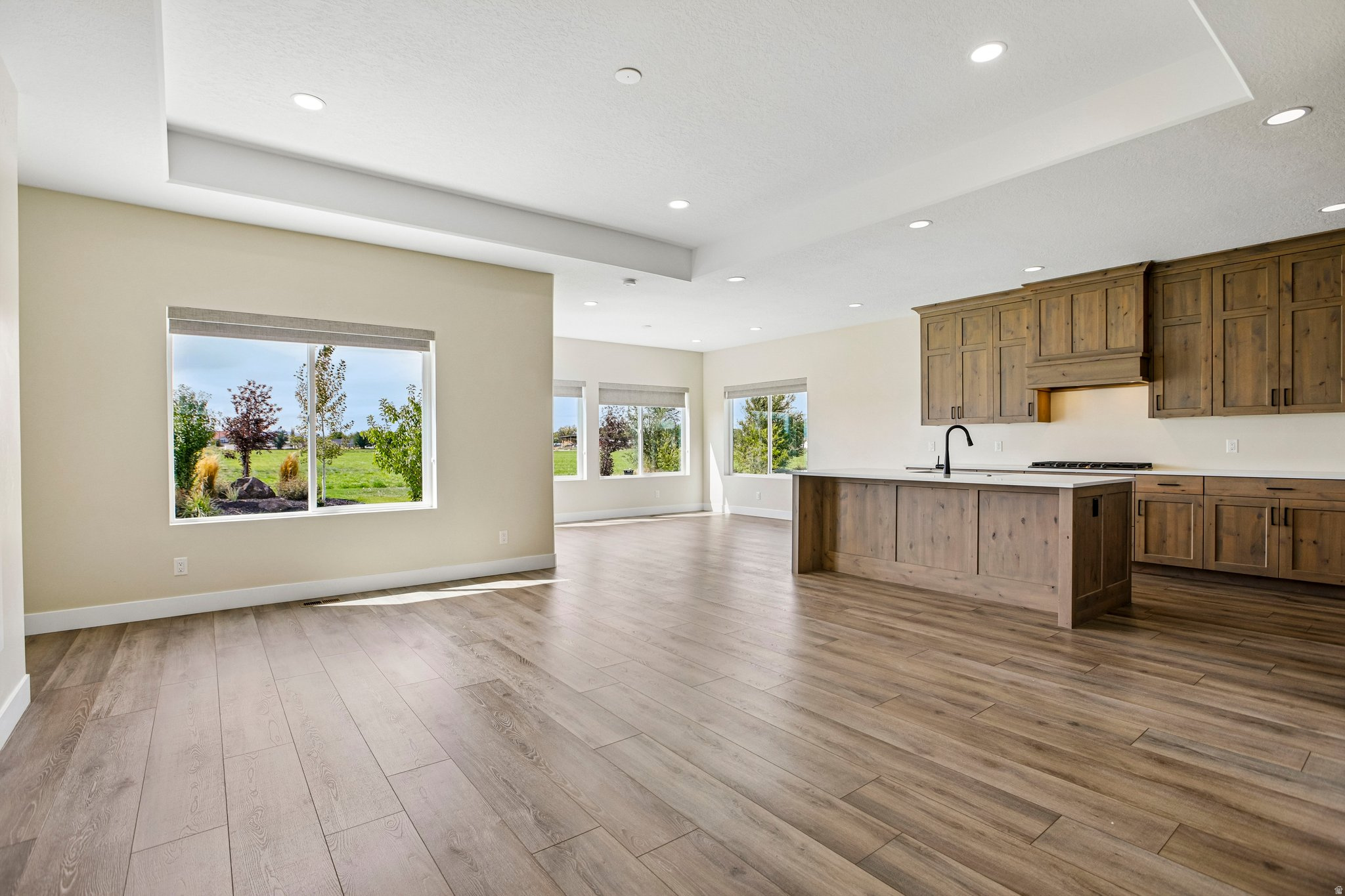 Expansive open-concept space featuring wood-finish flooring, a kitchen island with a built-in sink, wood cabinetry, and recessed lighting