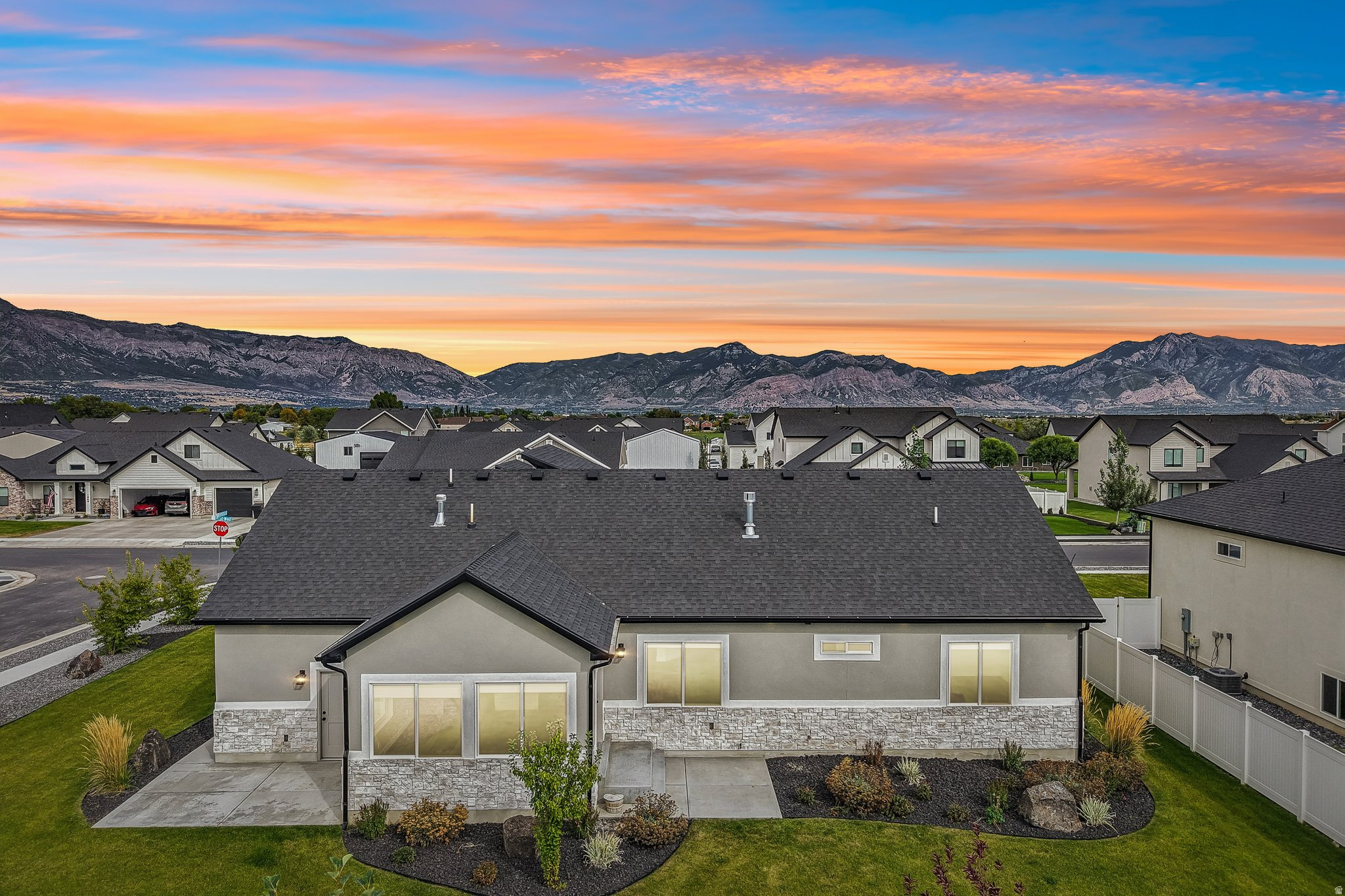 Stucco exterior with stone accenting, dark shingle roof, established landscaping, manicured lawn, and mountain scenery