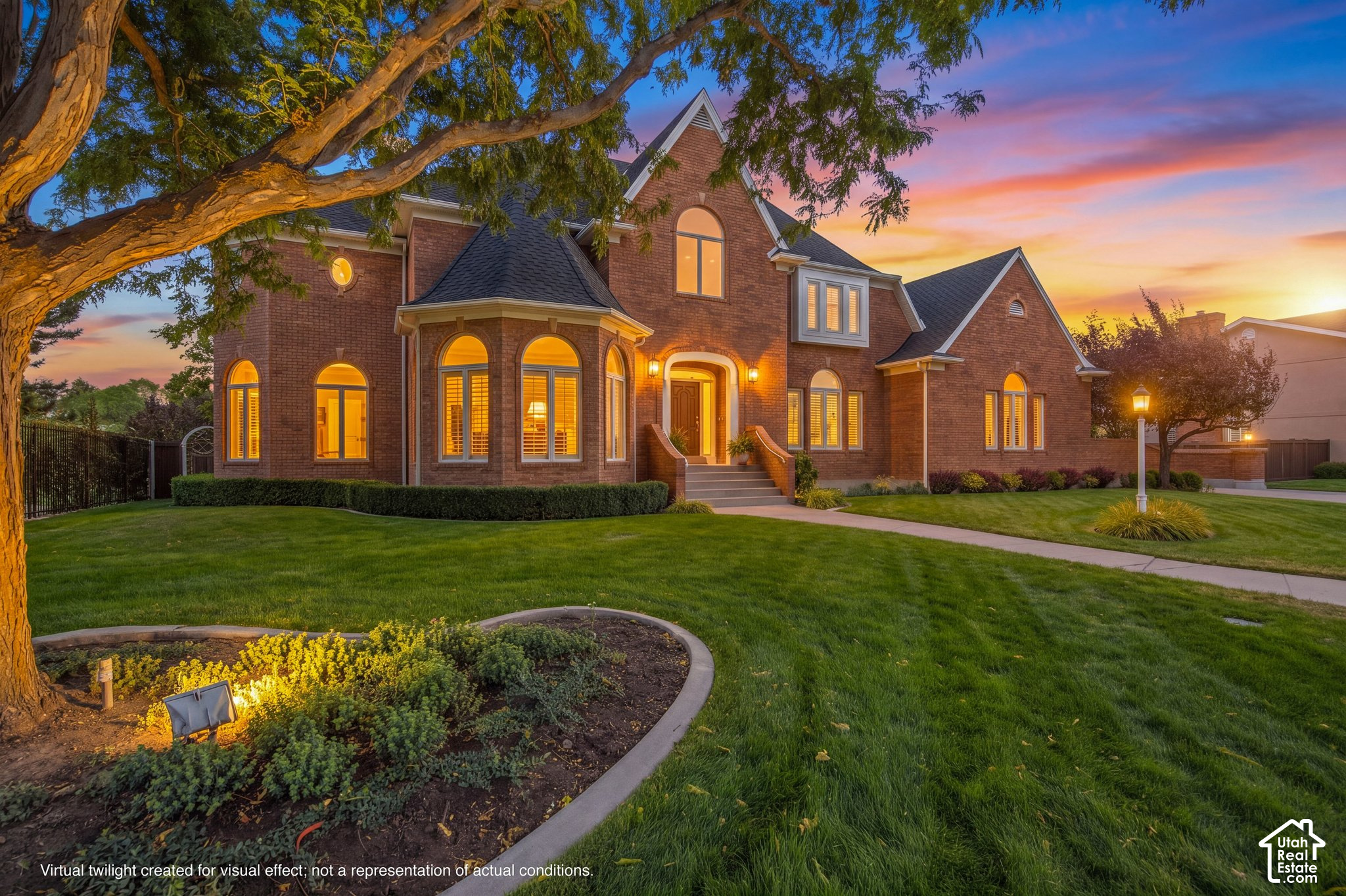 Large brick house with arched windows and a broad lawn, shown at sunset beneath a mature tree.