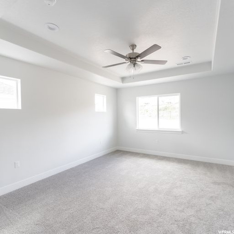 Carpeted empty room featuring a tray ceiling and ceiling fan