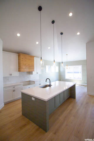 kitchen with natural light, light parquet floors, pendant lighting, light countertops, and a kitchen island with sink