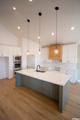 kitchen with a center island, vaulted ceiling, stainless steel microwave, oven, light countertops, white cabinets, light hardwood floors, and pendant lighting