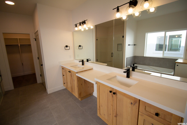 bathroom with tile floors, double large vanities, dual sinks, a bath, dual mirrors, and shower door