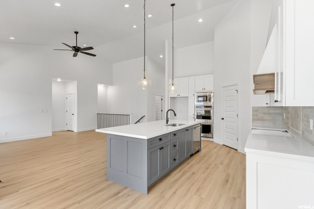 kitchen featuring microwave, oven, white cabinetry, a center island with sink, light countertops, pendant lighting, and light hardwood flooring