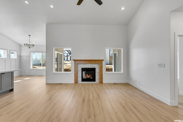 hardwood floored living room featuring natural light, lofted ceiling, a ceiling fan, and a fireplace