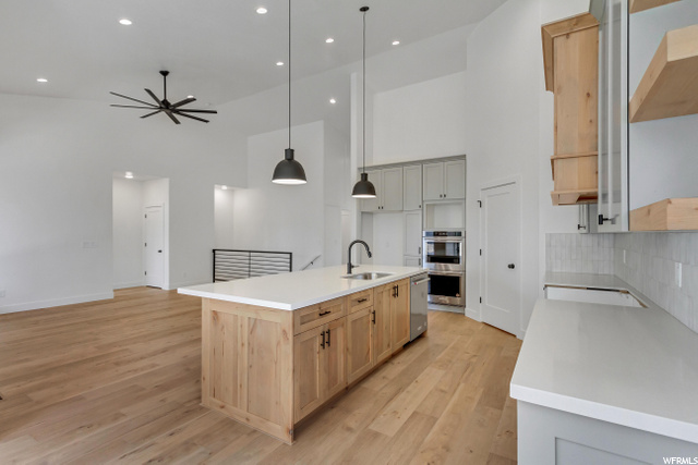 kitchen featuring double oven, dishwasher, light parquet floors, pendant lighting, a center island with sink, and light countertops