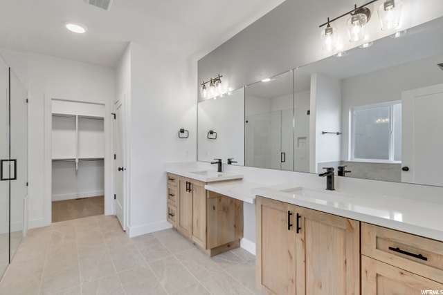 bathroom featuring tile flooring, shower door, dual mirrors, and double vanities