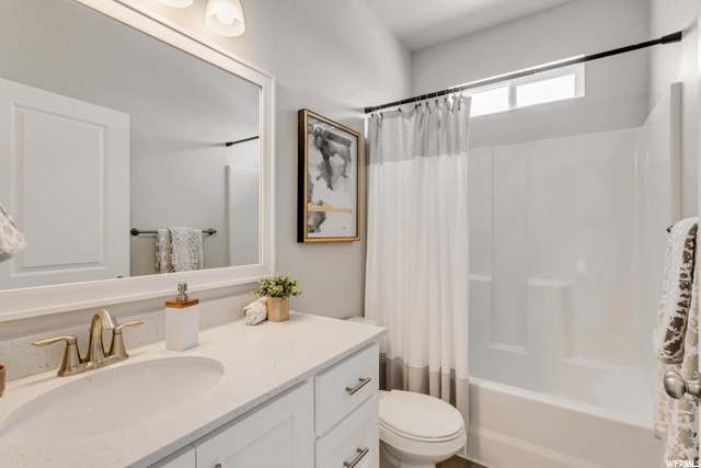 full bathroom with toilet, shower curtain, large vanity, bathtub / shower combination, and mirror