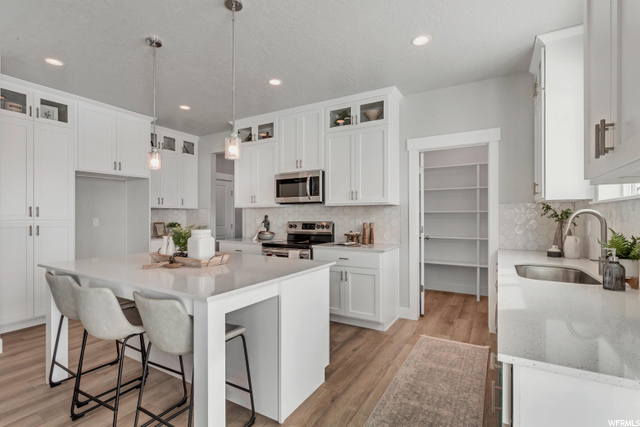 kitchen featuring a kitchen bar, range oven, stainless steel microwave, pendant lighting, white cabinetry, light countertops, and light hardwood flooring
