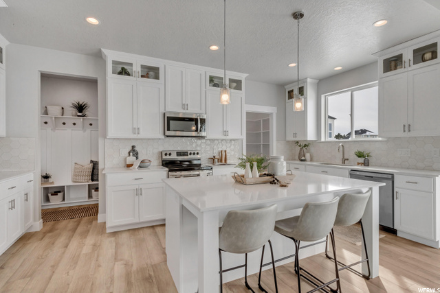 kitchen with a kitchen island, a breakfast bar area, dishwasher, electric range oven, microwave, pendant lighting, light hardwood floors, light countertops, and white cabinets