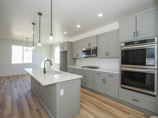kitchen featuring wood-type flooring, natural light, gas stovetop, microwave, stainless steel double oven, light countertops, pendant lighting, and white cabinets