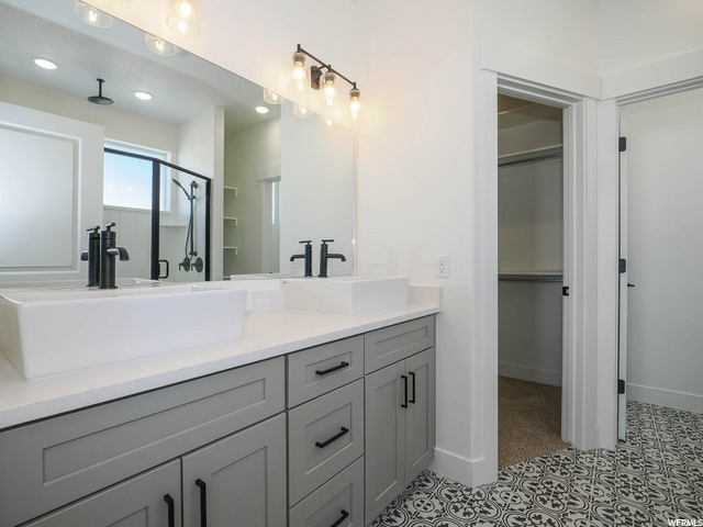 bathroom featuring mirror, his and hers large vanity, and shower door