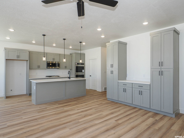 kitchen with double oven, microwave, light countertops, white cabinetry, light hardwood flooring, and pendant lighting