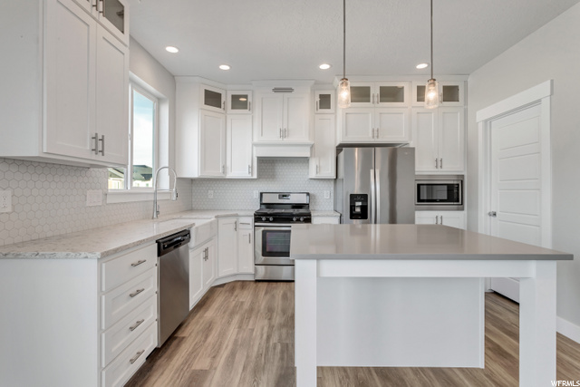 kitchen featuring natural light, range oven, refrigerator, stainless steel dishwasher, microwave, light hardwood floors, pendant lighting, white cabinetry, and light countertops