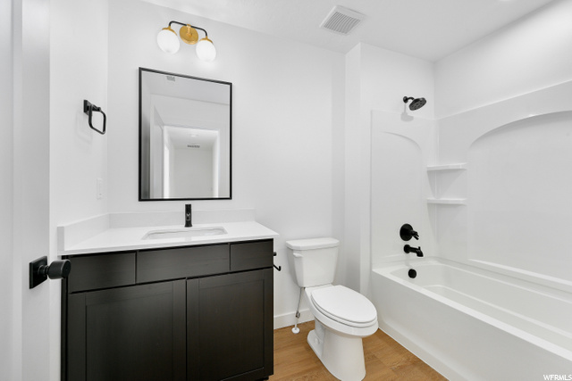 full bathroom featuring hardwood flooring, toilet, vanity, mirror, and shower / bath combination