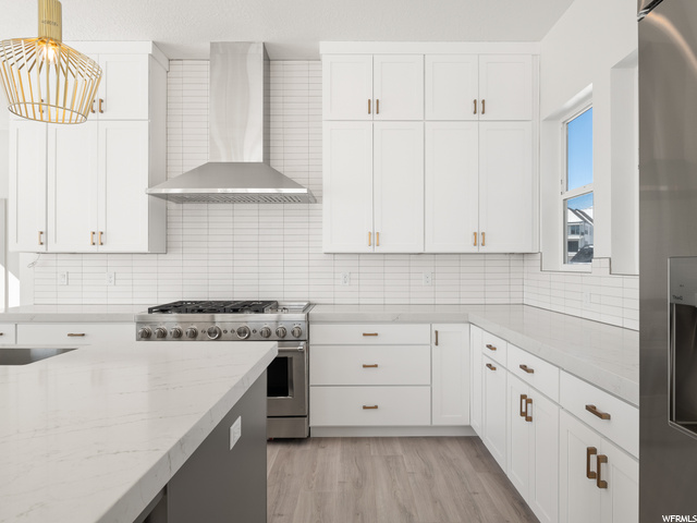 kitchen with range hood, stainless steel finishes, gas range oven, light parquet floors, white cabinets, and light countertops