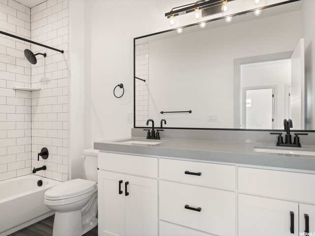 full bathroom featuring dual sinks, bathing tub / shower combination, double large vanities, toilet, and mirror