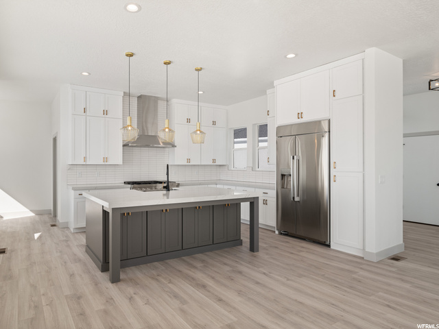 kitchen featuring a center island, refrigerator, ventilation hood, gas stovetop, pendant lighting, white cabinetry, light countertops, and light parquet floors