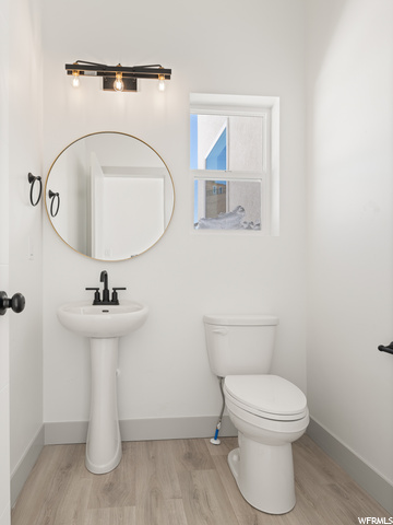 half bathroom featuring hardwood flooring, toilet, sink, and mirror
