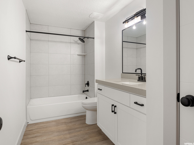 full bathroom featuring hardwood floors, toilet, tub / shower combination, vanity with extensive cabinet space, and mirror