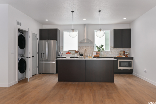 kitchen with refrigerator, independent washer and dryer, extractor fan, dark brown cabinetry, light countertops, light hardwood floors, and pendant lighting