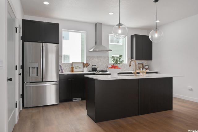 kitchen featuring natural light, refrigerator, fume extractor, pendant lighting, light countertops, dark brown cabinets, kitchen island sink, and light hardwood floors