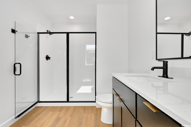 full bathroom with hardwood flooring, toilet, vanity, mirror, and shower with glass door