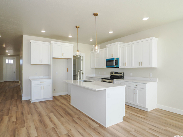 kitchen featuring a center island, range oven, microwave, light countertops, white cabinets, light hardwood flooring, and pendant lighting