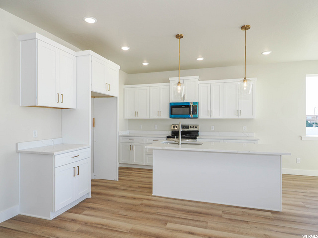 kitchen with range oven, microwave, light countertops, white cabinetry, light hardwood flooring, and pendant lighting